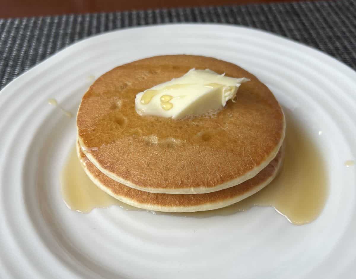 Image of a stack of three pancakes with butter and syrup on them served on a white plate.