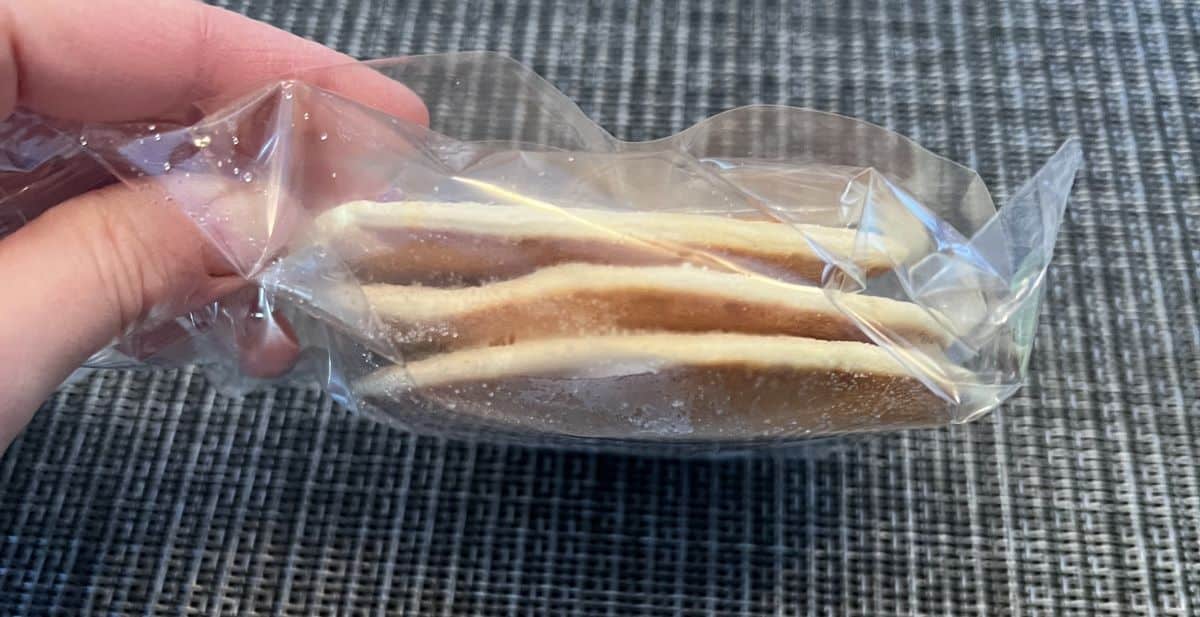 Image of a hand holding one unopened package of three frozen pancakes.