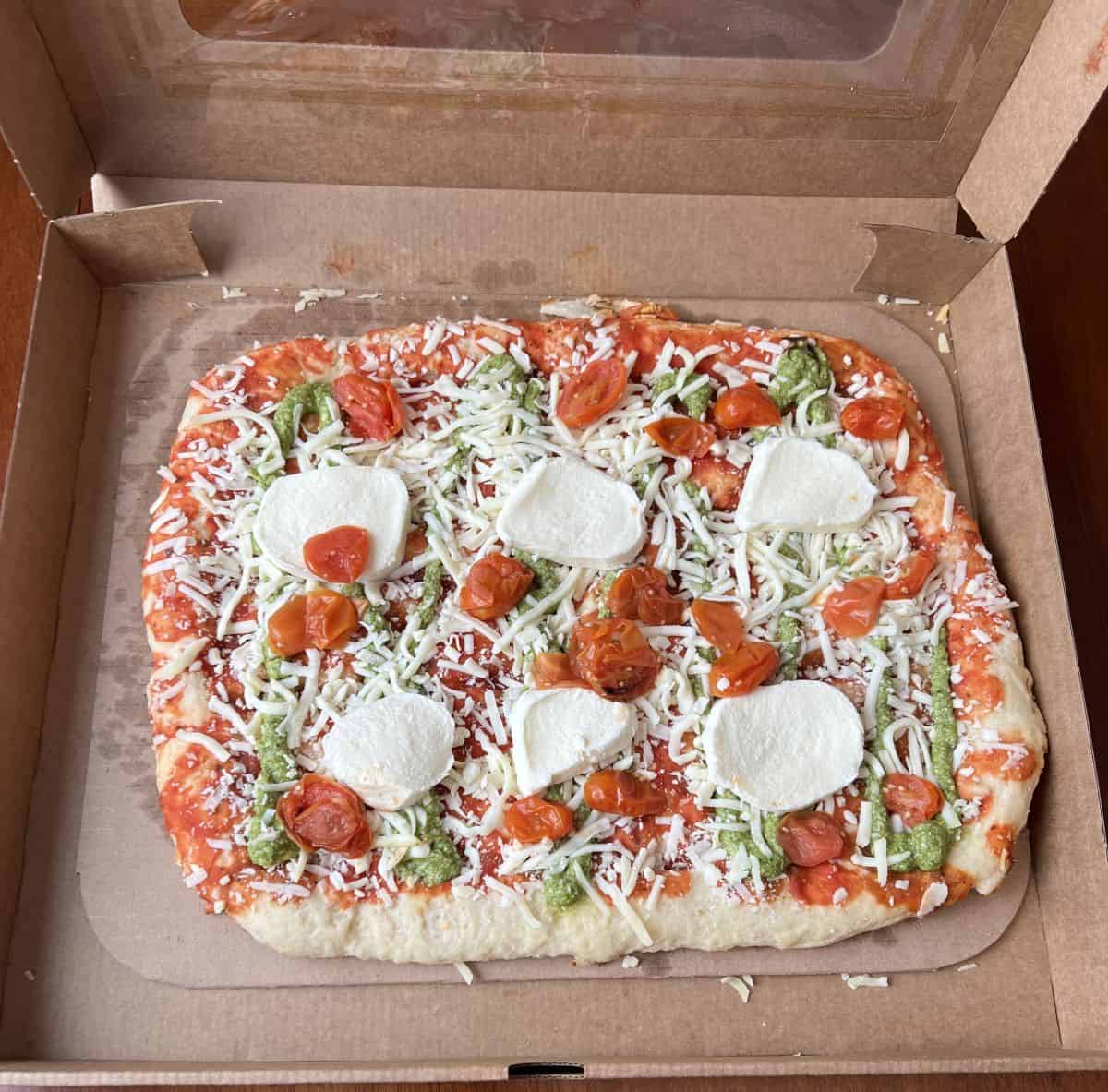 Image of the Costco Kirkland Signature Margherita Pinsa sitting in the box on a table opened so you can see the unbaked pizza.