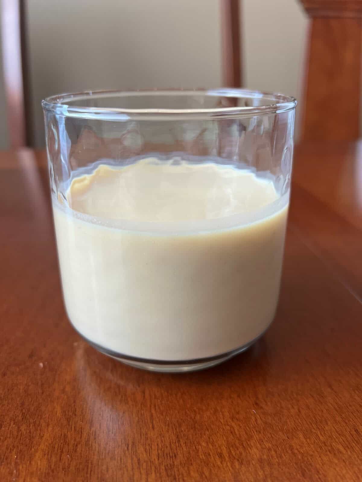 Image of a clear glass with protein shake in it sitting on a table.