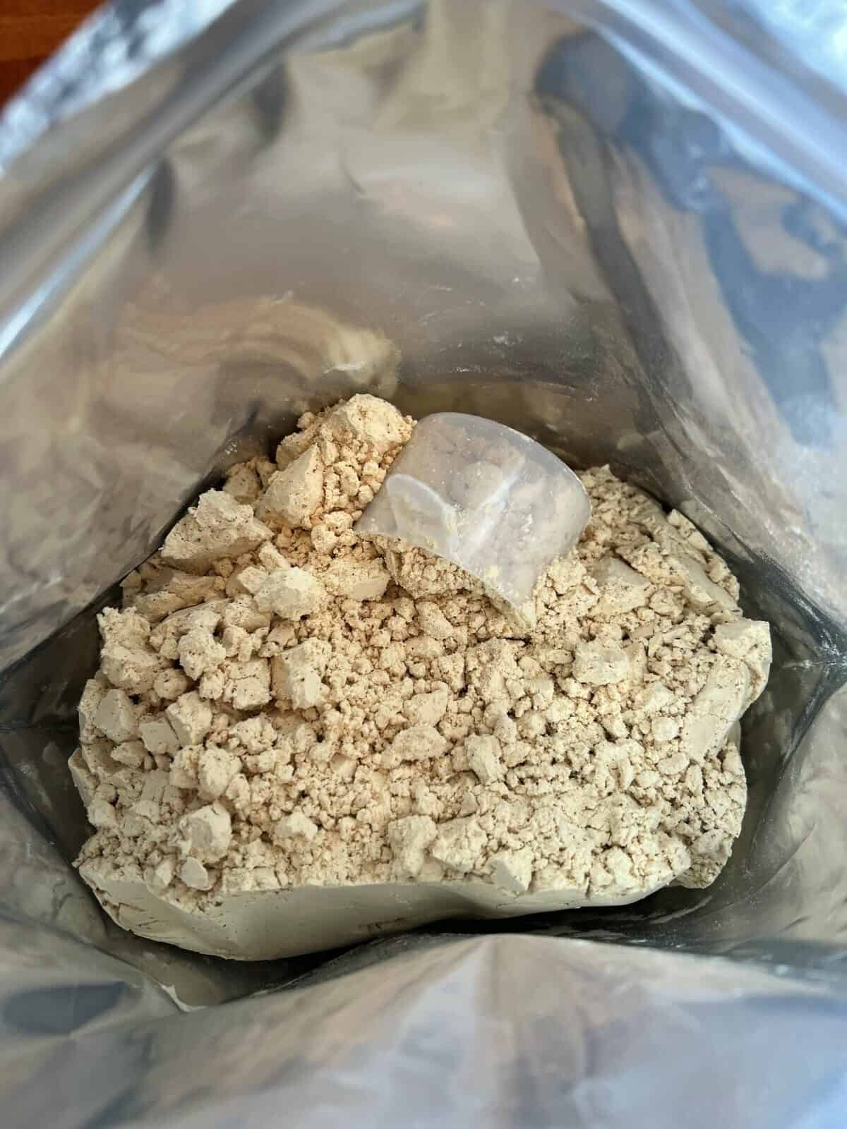 Top down image of an open bag of protein powder showing the protein powder and scoop in the bag.