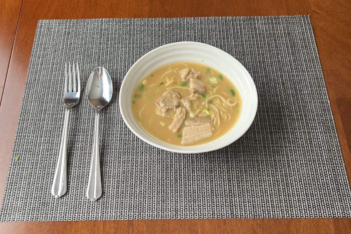 Image of a bowl of the Costco Pulmuone Tonkotsu Miso Ramen served on a table beside a fork and spoon.