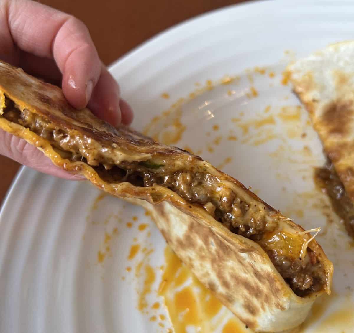 Image of a hand holding one piece of quesadilla close to the camera so you can see the filling inside.