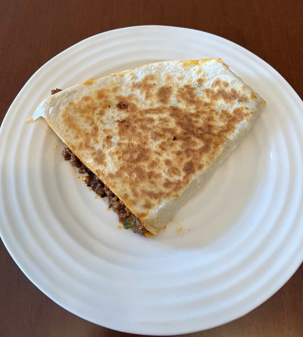 Image of one large quesadilla piece cooked and served on a white plate.