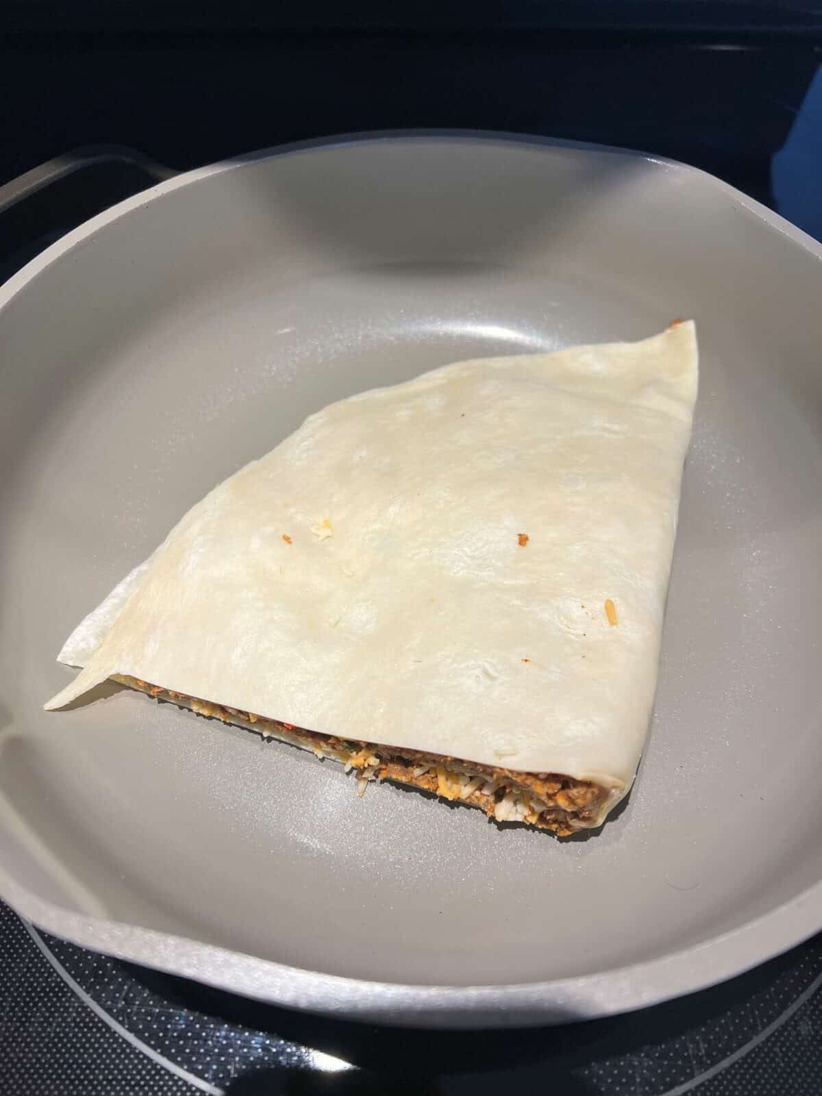 Image of an uncooked quesadilla being heated in a pan.