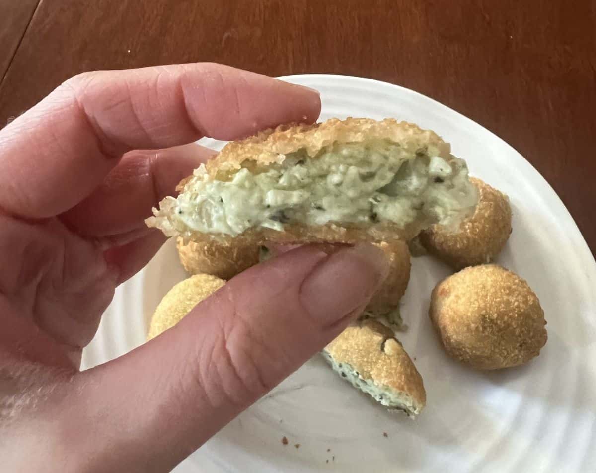 Image of a hand holding one spinach and artichoke bite cut in half so you can see the middle.