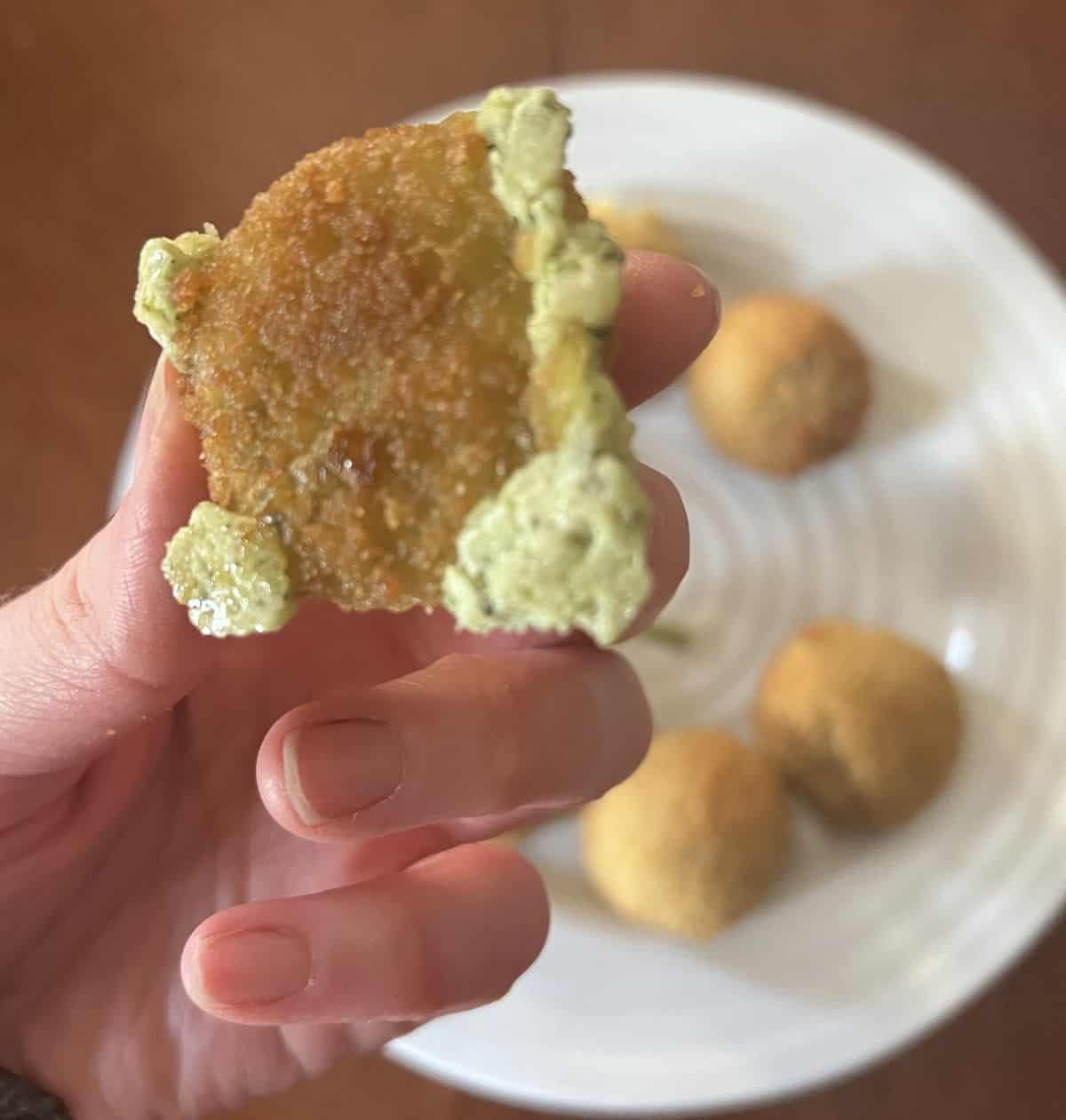 Image of one spinach & artichoke bite being held and some of the filling is oozing out of it.