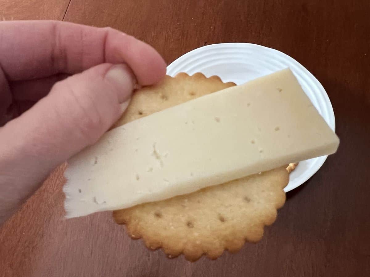 Image of a hand holding a cracker with a slice of manchego cheese on top of the cracker.