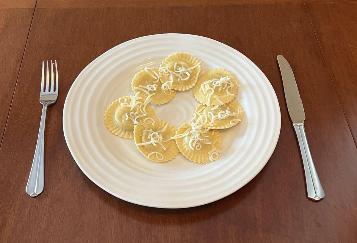 Image of seven ravioli served on a white plate with parmesan sprinkled on top. 