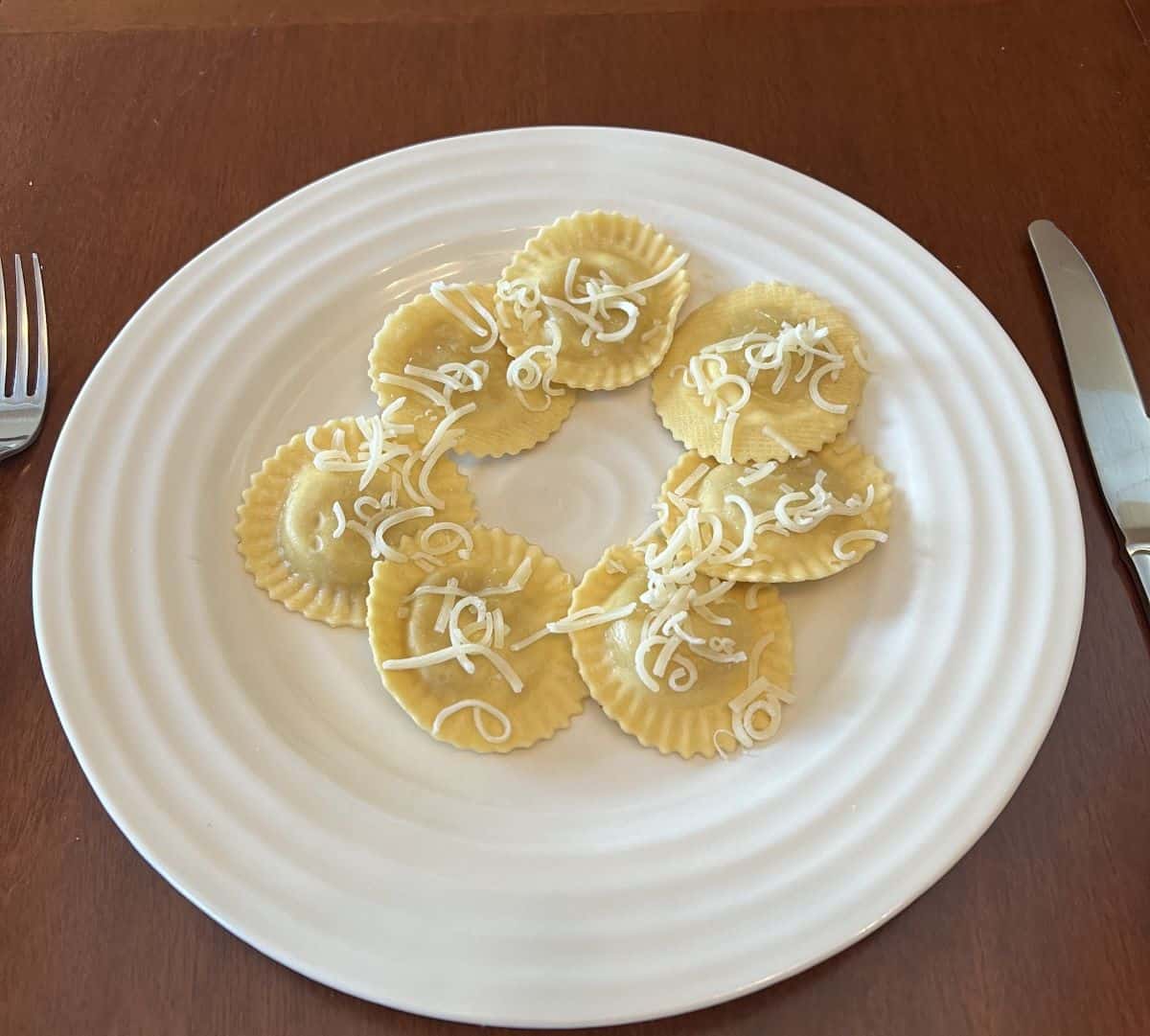 Close up image of ravioli served on a white plate with butter sauce and parmesan sprinkled on top.