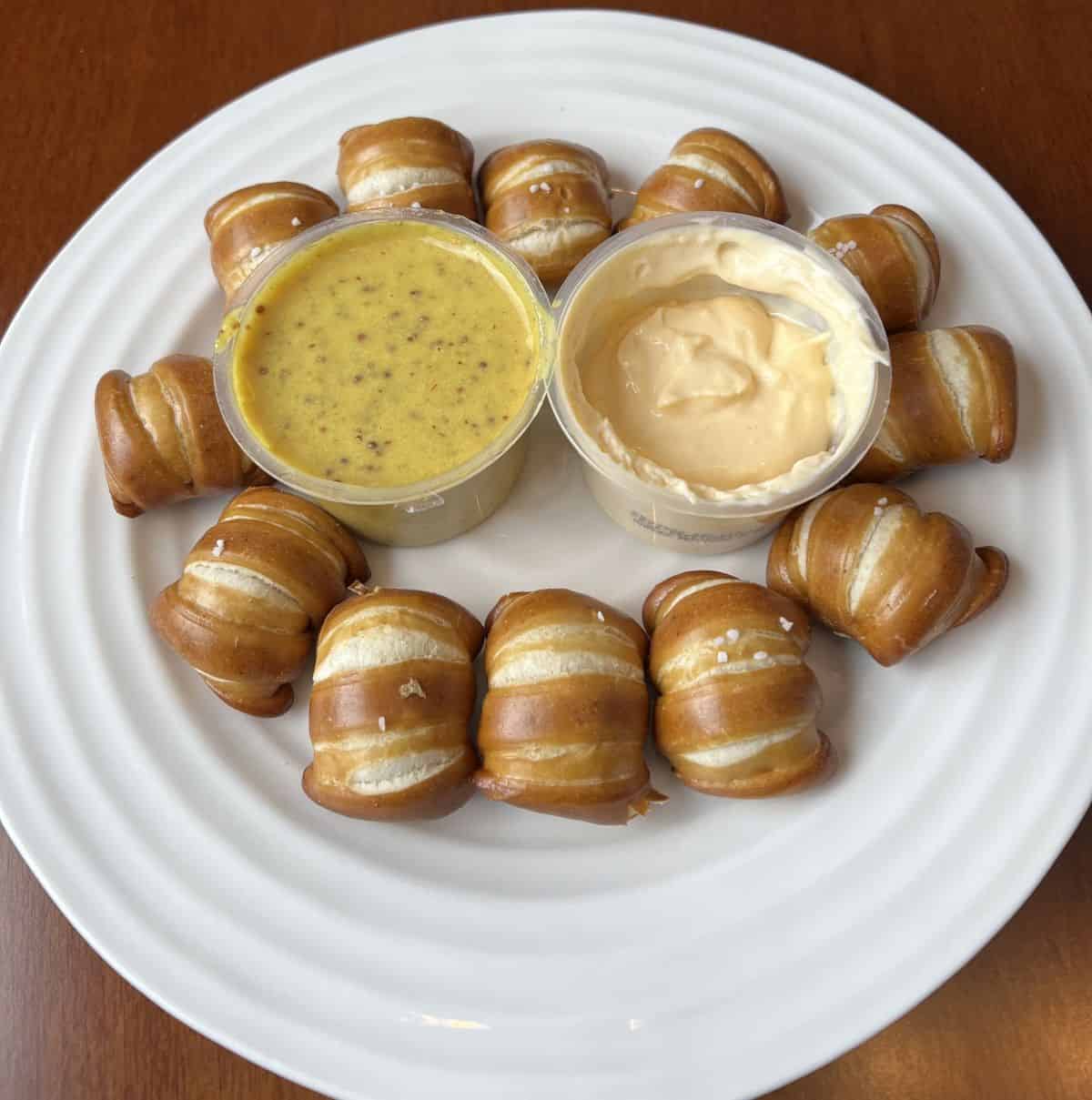 Top down image of a plate of pretzel bites with a cheese dip and mustard dip in the middle of the plate.