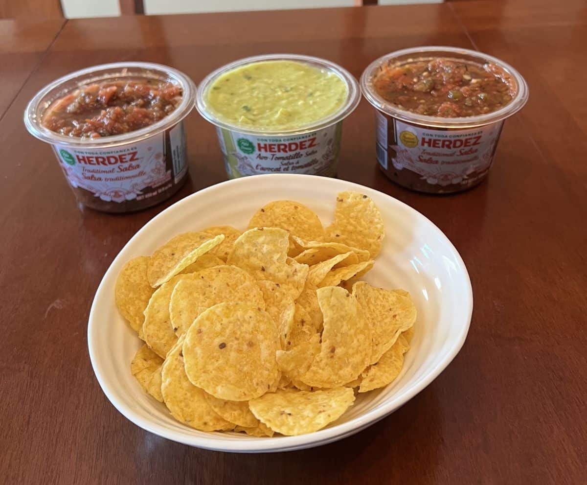 Image of a bowl of tortilla chips beside three open containers of salsa.