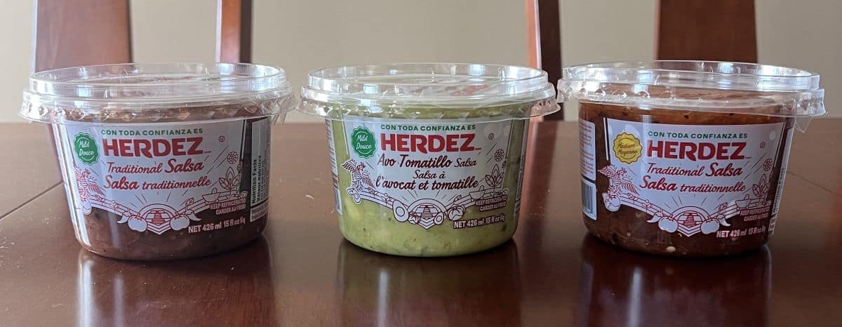 Image of three different kinds of salsa containers sitting on a table unopened.